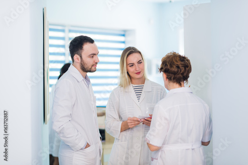 Mature doctor discussing with nurses in a hallway hospital. Doctor discussing patient case status with his medical staff after operation. © romankosolapov