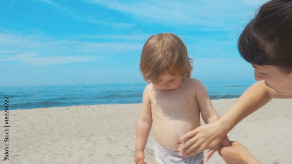 Mother applying sunscreen lotion on son back at beach. Mother preparing child for bath in sea. Mother applying sunscreen lotion on son back at beach. Mother preparing child for bath in sea.