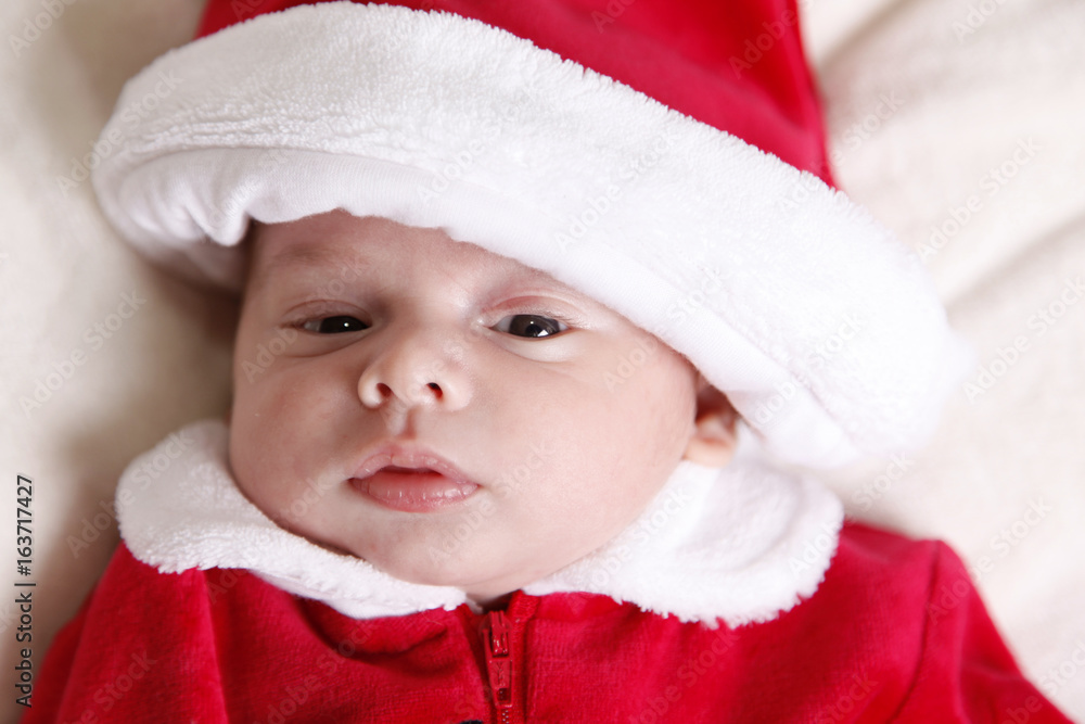 tiny newborn in santa claus suit / a close up portrait of a newborn infant is dressed in a red and white santa suit with hat in studio tiny newborn in santa claus suit / a close up portrait of a newborn infant is dressed in a red and white santa suit with hat in studio