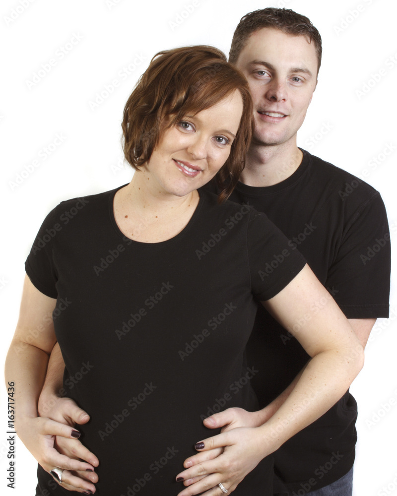 a young couple in studio with man behind holding wife's belly a young couple in studio with man behind holding wife's belly
