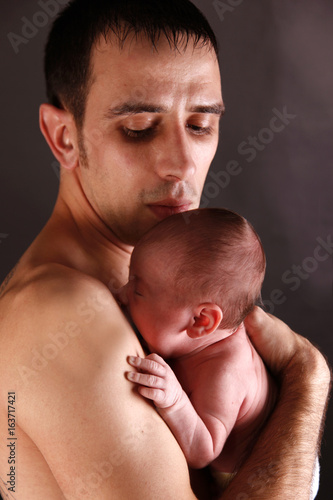 an infant is held by his father with skin on skin contact, studio background 