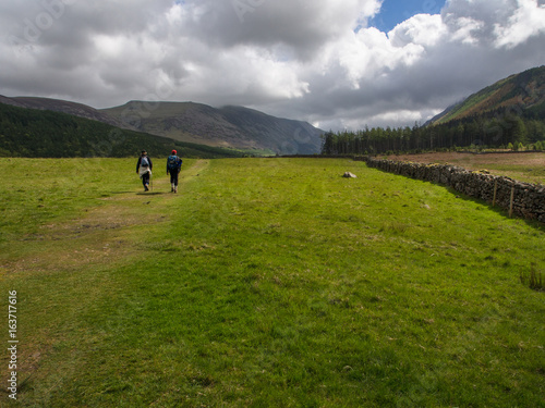 Hikers on trail across meadow, Cumbria, England © Alan
