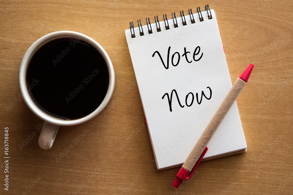 Vote now handwriting on notebook with cup of coffee. Vote now handwriting on notebook with cup of coffee.