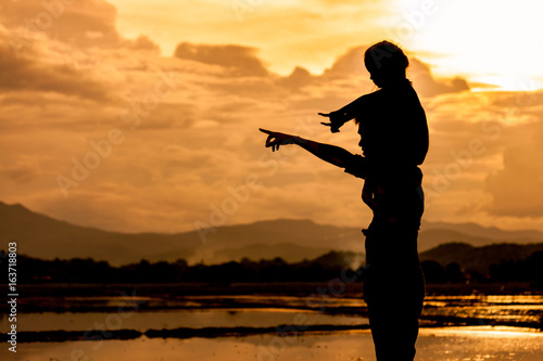 Silhouette asian little girl riding on father's shoulder and playing together with sky and cloudy in the cornfield at sunset