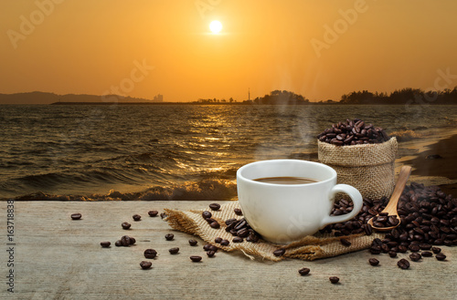 Hot Coffee cup with Coffee beans on the wooden table and the sea background