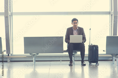 Asian Indian business man sitting on chair and using laptop while waiting his flight at airport.