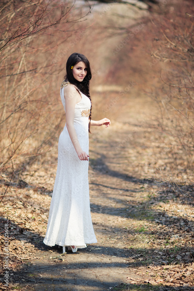 Bride with flowers in hair walking along the path in the forest. Woman in white dress posing on wedding photo session. Bride with flowers in hair walking along the path in the forest. Woman in white dress posing on wedding photo session.