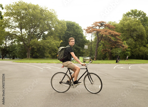 Fototapeta Naklejka Na Ścianę i Meble -  Full figure shot of modern Caucasian college student riding bike in the park