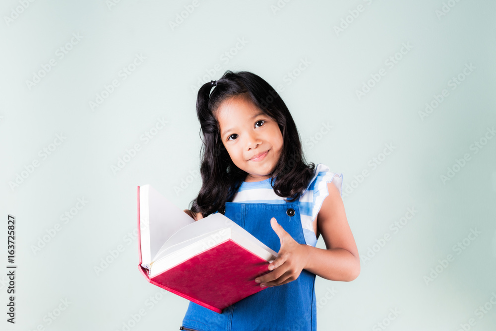 happy smiling asian little girl reading a red book with white concrete wall background..concept of education for child happy smiling asian little girl reading a red book with white concrete wall background..concept of education for child