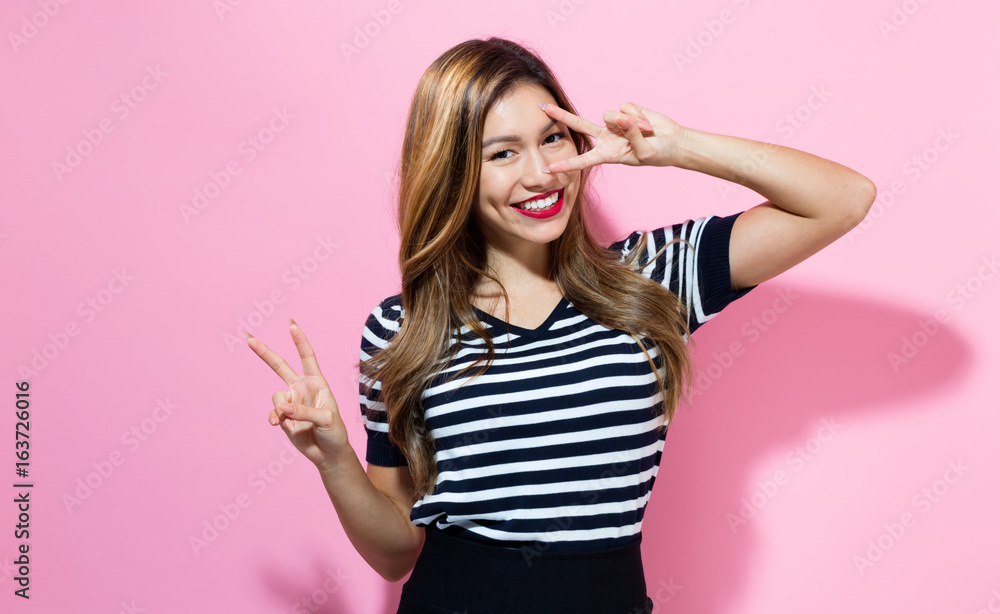 Young woman giving the peace sign on a pink background Young woman giving the peace sign on a pink background