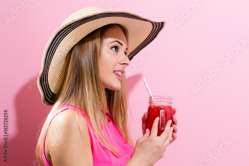 Happy young woman drinking smoothie on a pink background