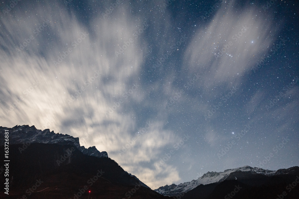Mountain with little snow on the top and moving cloud in the blue color night with stars in winter at Lachung in North Sikkim, India.