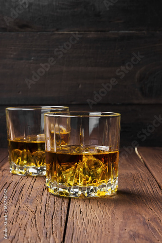 Whisky with ice in two glasses on a wooden background