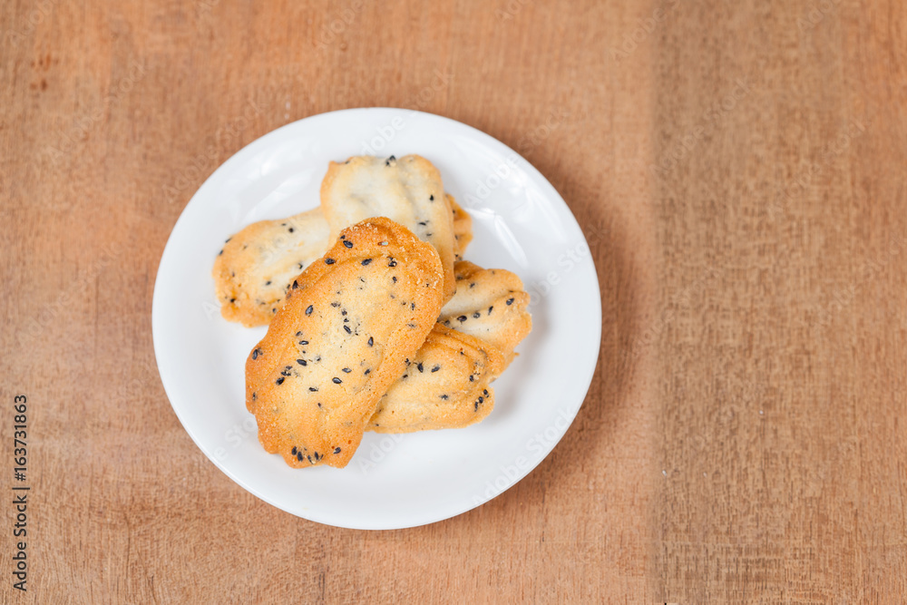 Home made a small sweet cookie with black sesame, typically round, flat, and crisp.Cookie in dish on wood. Home made a small sweet cookie with black sesame, typically round, flat, and crisp.Cookie in dish on wood.