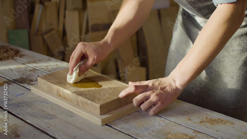 Fotografi Portrait of 20s bearded carpenter woodworker rubs lacquer in a wooden plank in t