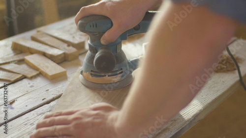 Hands of woodworker carpenter grinding wooden plank in backlight using machine