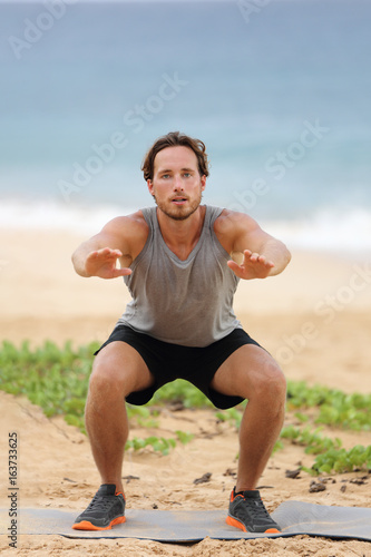 Squat exercise fitness man training squats for glutes and quadricep muscles doing workout burpees working out beach in summer outdoors.