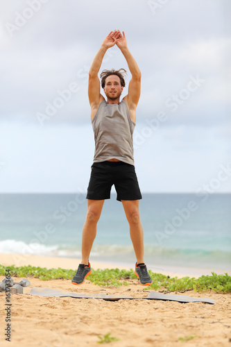 Jump Squats fitness training. Athlete Man doing Jump Squat exercise workout. Male fitness instructor training on beach. photo