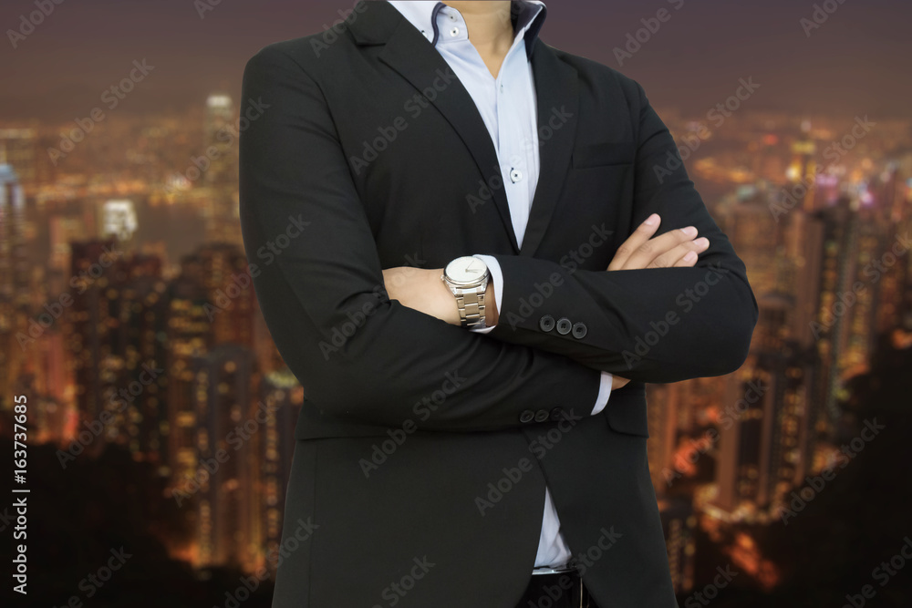 Business man wearing business suit with arms crossed on blur night city background Business man wearing business suit with arms crossed on blur night city background