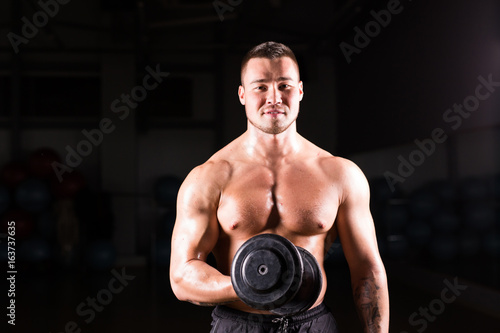 Muscular man working out in gym doing exercises with dumbbells at biceps, strong male naked torso abs.