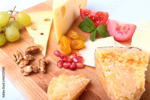 Assortment of cheese with fruits, grapes, nuts and cheese knife on a wooden serving tray. photo