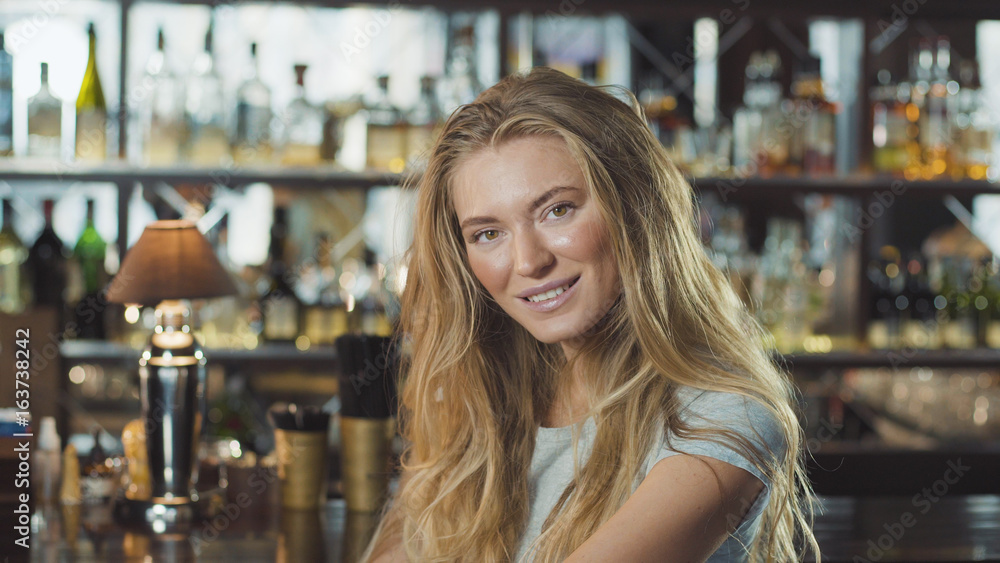 Beautiful blonde woman in evening dress sitting near bar counter and looking at camera Beautiful blonde woman in evening dress sitting near bar counter and looking at camera