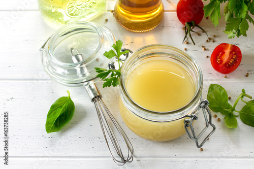 Photography Homemade salad dressing vinaigrette with mustard, olive oil, lemon juice and various fresh vegetables and herbs on a wooden background
