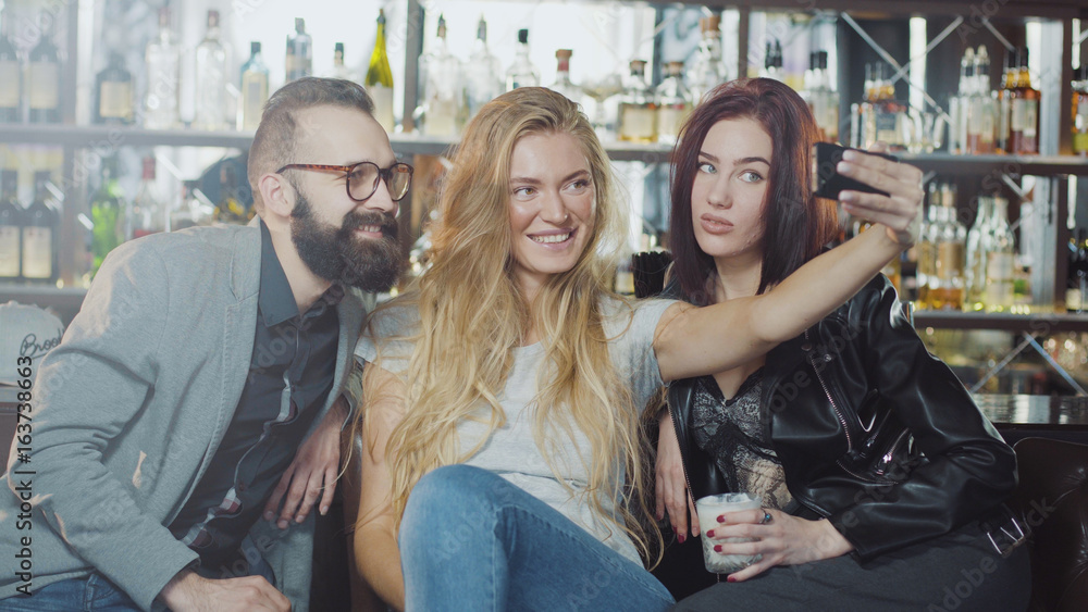 3 person company of friends are taking selfie behind bar counter, smiling and looking at smartphone camera with happy emotions faces 3 person company of friends are taking selfie behind bar counter, smiling and looking at smartphone camera with happy emotions faces