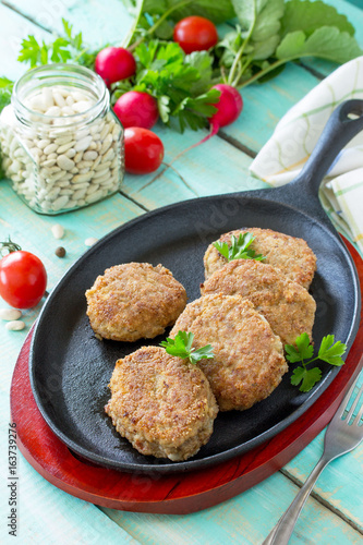 Domestic meat cutlet with white beans and fresh herbs. Cast-iron frying pan full of delicious fried meat cutlets, fresh greens and vegetables on the kitchen table.