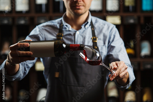 Male sommelier pouring red wine into long-stemmed wineglasses.