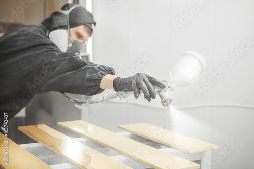 Schilderij op canvas Man in respirator mask painting wooden planks at workshop.