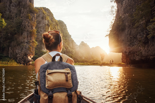 woman with backpack traveling by boat enjoying sunset among of mountains. photo