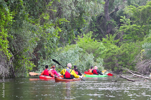 Group of people (friends) kayaking in wild river and lake on biosphere reserve in spring on cloudy spring day