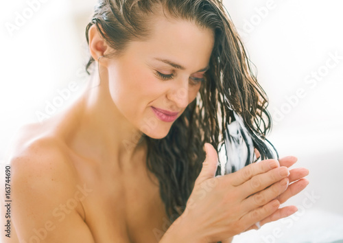 Tableau sur toile Happy young woman applying hair conditioner in bathtub