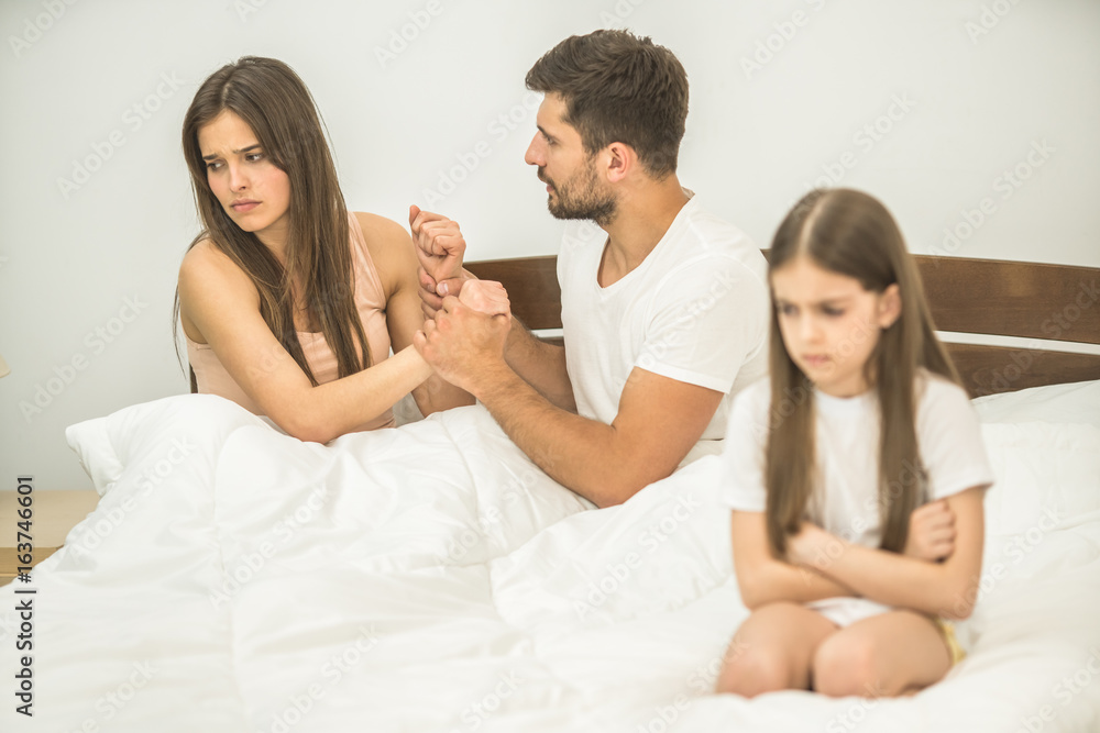 The parents fighting near the sad daughter on the bed The parents fighting near the sad daughter on the bed