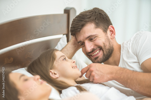 The happy father lay near the family in the bed