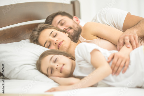 The daughter and parents sleeping in the bed