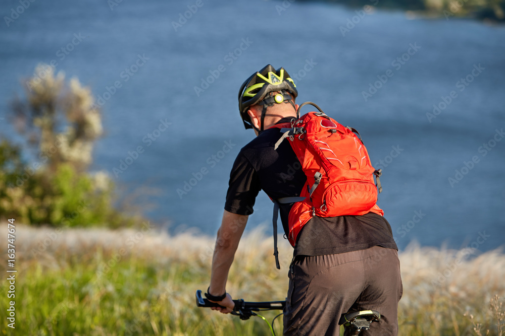 Young man riding mountain bike on the green meadow above the blue river in the countryside. Young man riding mountain bike on the green meadow above the blue river in the countryside.