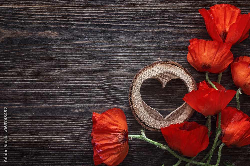 Obraz premium Czerwone maki kwiaty z drewnianym sercem na ciemnym tle drewna.