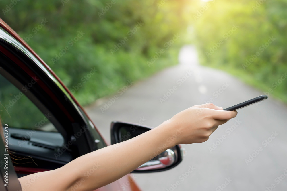 Young woman holding using smartphone while stop driving car on the road.