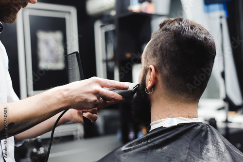 Young handsome barber making haircut of attractive man in barbershop