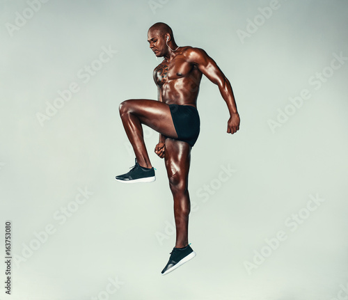 Fitness man jumping and stretching over grey background