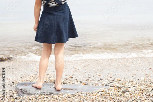 Little girl standing on pebble beach at sea shore. Lower body of female child at the beach.