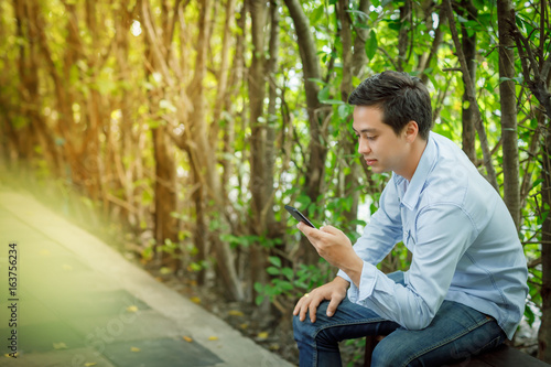 Middle aged Asian men sit on a wooden bench in the garden. And are playing mobile phones.