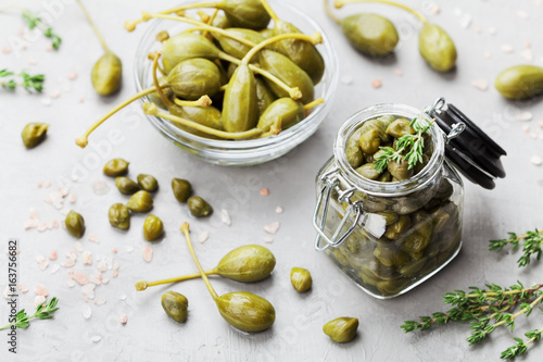 Mixed capers in jar and bowl on gray kitchen table from above. photo