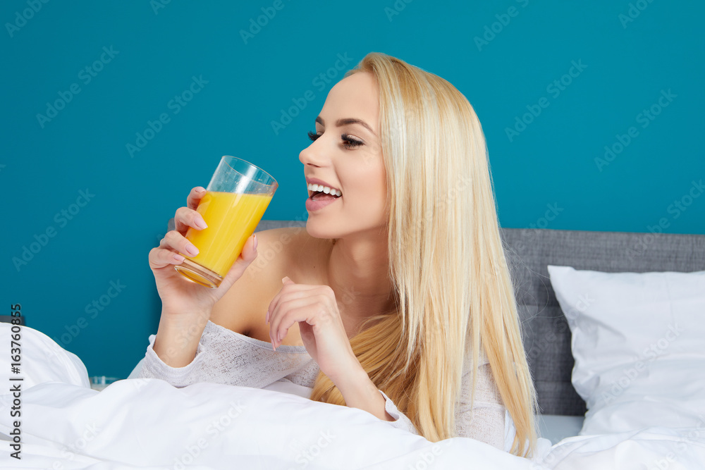 Attractive woman drinking orange juice sitting on her bed Attractive woman drinking orange juice sitting on her bed