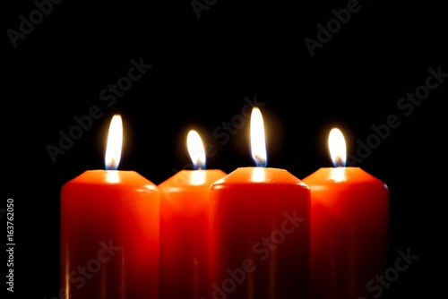 Closeup of four burning candles isolated on black. One candle in focus