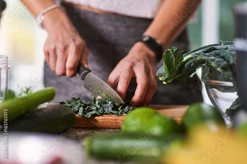 Hands of young woman slicing cabbage at kitchen table photo