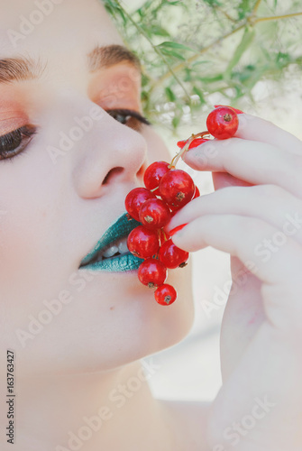 blonde woman with green lips holding red currants bunch