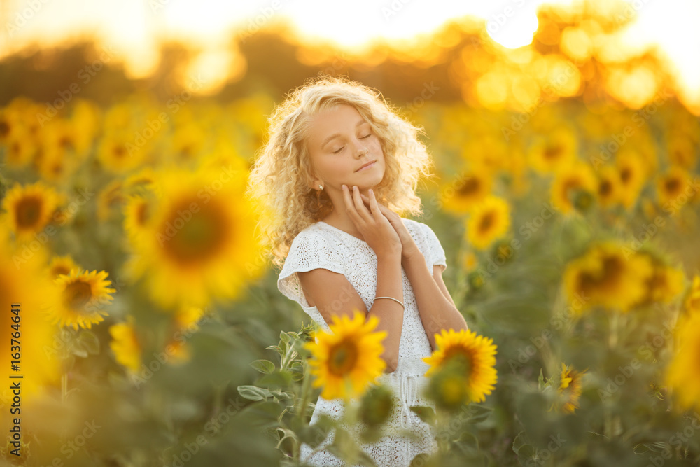 Pretty curly girl in white dress in filed of sunflowers over sunset lights Pretty curly girl in white dress in filed of sunflowers over sunset lights
